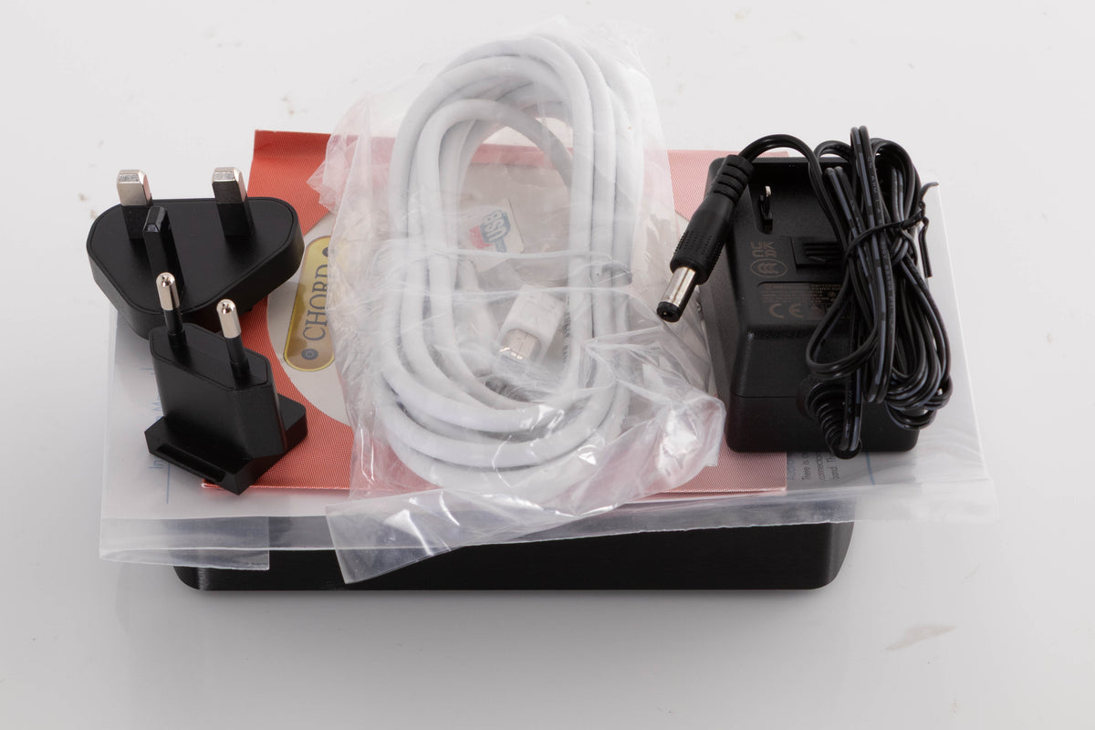 Top of a used Chord Electronics Qute HD Digital Analogue Converter in a Black finish showing PSU, Mains Plug, Schuko Plug, USB Cable and Manual