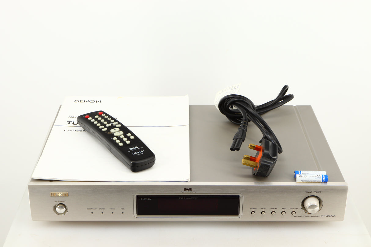 Top of a used Denon TU-1800 DAB/FM Tuner in a silver finish showing Manual, Power Cable, Remote and 2x Batteries