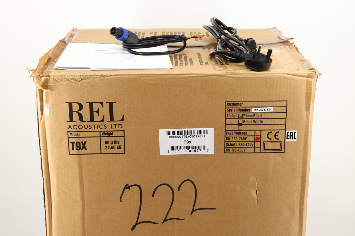 Box of a used REL T9X Subwoofer in Piano Black finish showing mains cable, manual, and Hi-Level cable