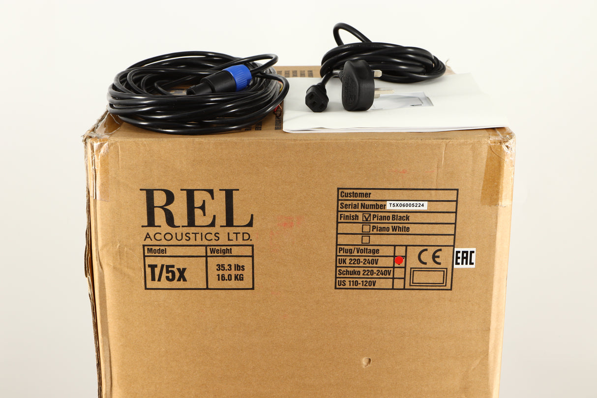 Box of a used REL T5X Subwoofer in Piano Black finish with mains cable, manual, and Hi level cable