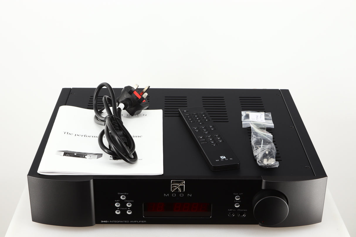 Top of a used Simaudio Moon 340i D3PX Integrated Amplifier in a black finish showing Manual, Battery, Remote, Mains Cable, Fuse and AUX Cable