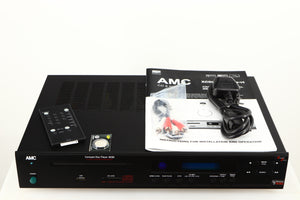 Top of a used AMC XCDise-vt CD Player With MD5404us2 Tube Output in a black finish showing Remote, Battery, Interconnect Cable, Mains Cable and Manual