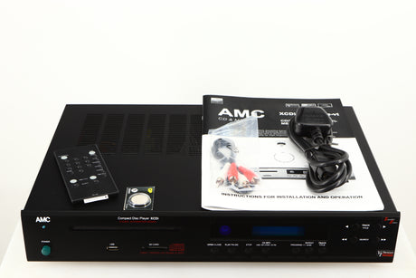 Top of a used AMC XCDise-vt CD Player With MD5404us2 Tube Output in a black finish showing Remote, Battery, Interconnect Cable, Mains Cable and Manual