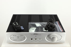Top of a used Astin Trew AT2-2100 Integrated Amplifier in a silver finish showing Remote, 2x Batteries, Manual and Mains Cable 