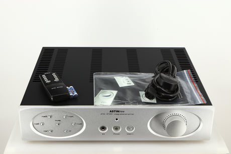 Top of a used Astin Trew AT2-2100 Integrated Amplifier in a silver finish showing Remote, 2x Batteries, Manual and Mains Cable 