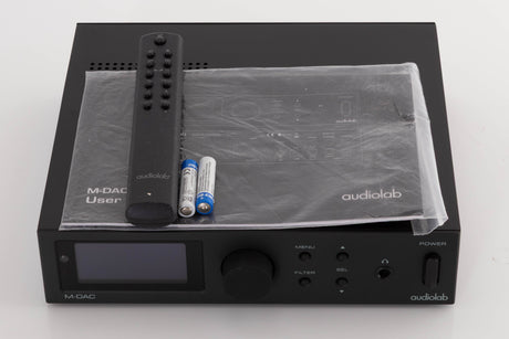 Top of a used Audiolab M-DAC Digital Analogue Converter in a Black finish showing Manual, Remote and Batteries