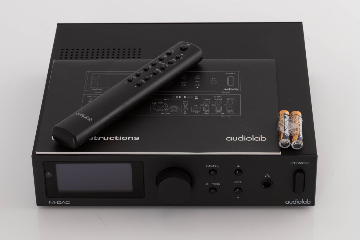 Top of a used Audiolab M-DAC Digital Analogue Converter in a Black finish showing Manual, Remote and Batteries