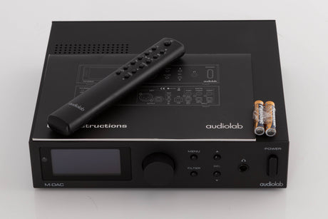 Top of a used Audiolab M-DAC Digital Analogue Converter in a Black finish showing Manual, Remote and Batteries