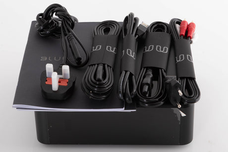 Top of a used Bluesound Node Icon Music Streamer in a Black finish showing Power Cable, Ethernet Cable, Interconnect Cable, Manual and Schuko Cables