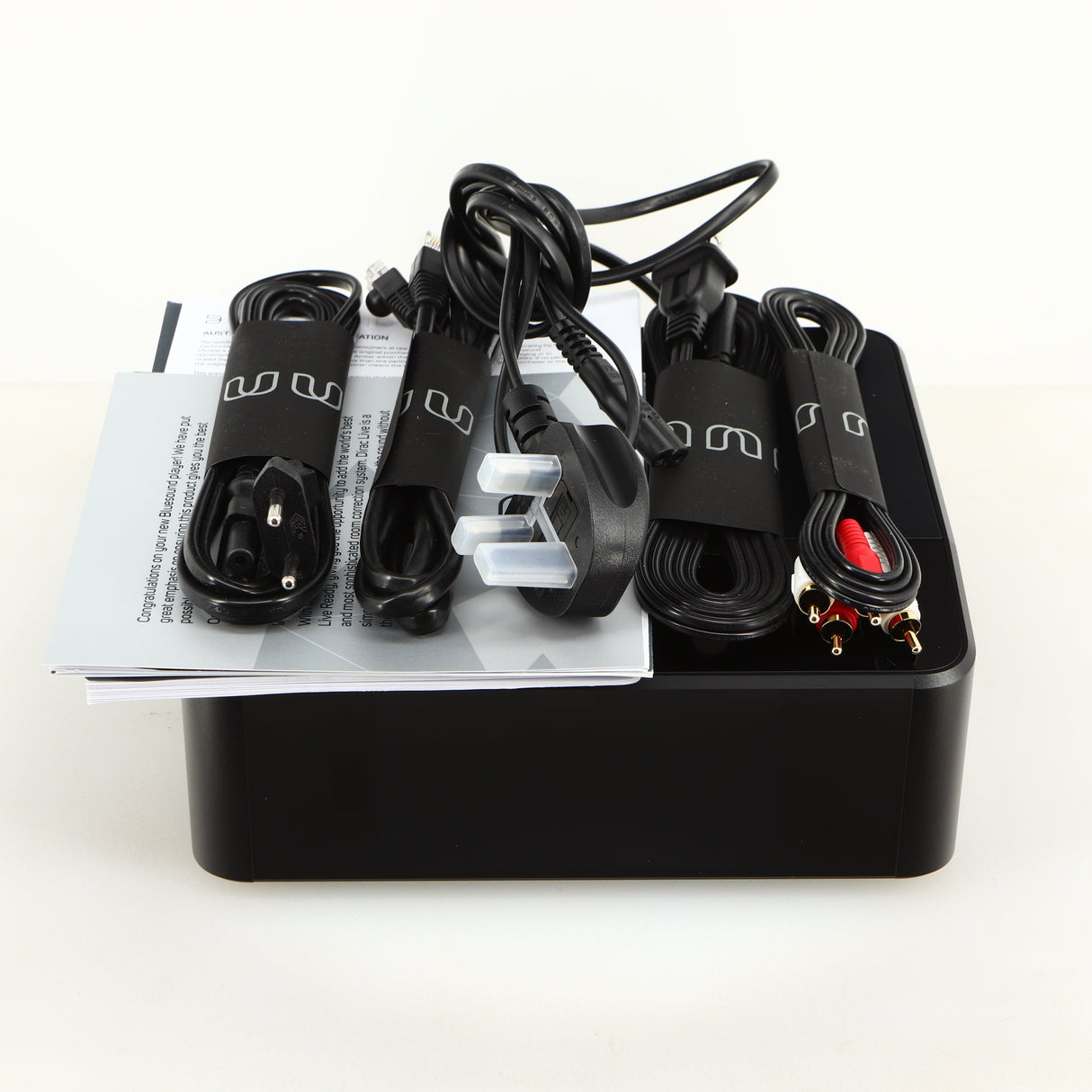 Top of a used Bluesound Node Icon Streamer in a black finish showing Manual, Warranty Card, Power Cable, Interconnect Cable, Ethernet Cable and Schuko Power Cable