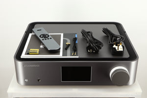 Top of a used Cambridge Audio Edge NQ Network Pre Amplifier in a grey finish showing Manual, Warranty Card, Remote, 3x Batteries, Mains Cable, Schuko Cable, Bluetooth Cable, AUX Cable