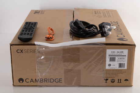 Box of a used Cambridge CXC CD Transport in Silver with mains cable, remote, and control bus cable