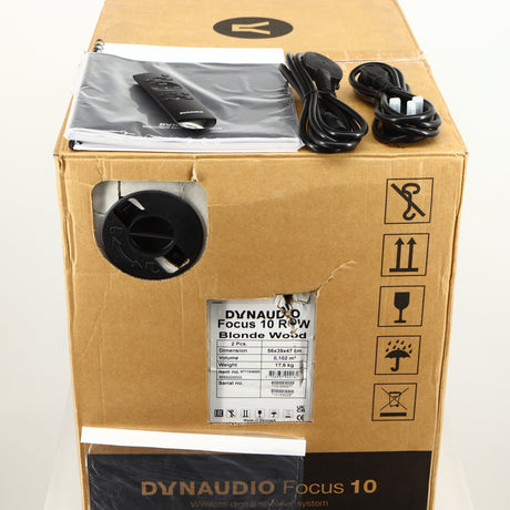 Box for a used Dynaudio Focus 10 Standmount Speaker in a blonde finish showing 2x Manuals, 2x Mains Cables, Remote and 2x Grilles