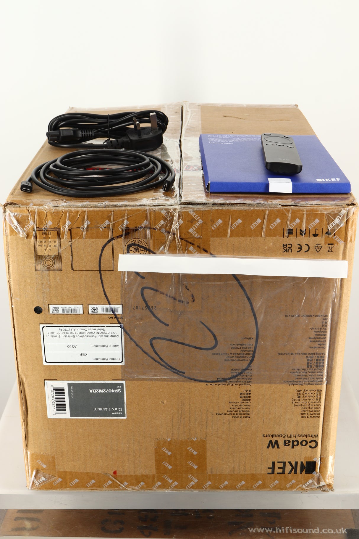 Box of a used KEF Coda W Active Standmount Speaker in Dark Titanium finish with mains cable, manual, remote, and USB-C cable