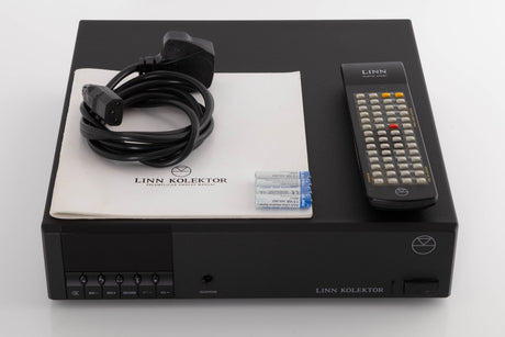 Top of a used Linn Kolektor Pre Amplifier in a Black finish showing Remote, Batteries, Manual and Mains Cable