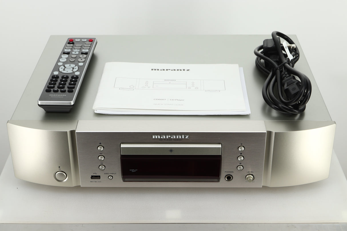 Accessories of a used Marantz CD6007 CD Player in silver finish showing a manual, remote, and mains cable