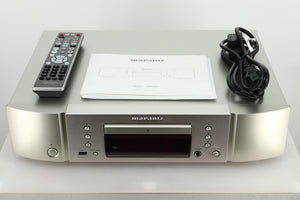 Accessories of a used Marantz CD6007 CD Player in silver finish showing a manual, remote, and mains cable