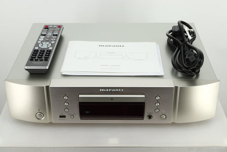 Accessories of a used Marantz CD6007 CD Player in silver finish showing a manual, remote, and mains cable