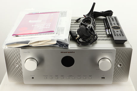 Top of a used Marantz Cinema 60 AV Receiver in a silver finish showing Manual, Microphone Stand, Microphone, Mains Cable, Remote, 2x Batteries, Wi-Fi Antenna and Bluetooth Antenna