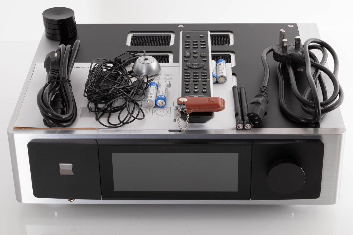 Top of a used NAD M33 V1 BluOS Streaming DAC Integrated Amplifier showing Remote, Batteries, USB Stick, Mains Cable, Schuko Cable, Manual, Microphone, Spare Feet, Wi-Fi Antenna and Bluetooth Antenna 