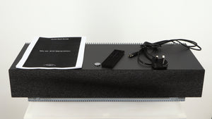 Top of a used Naim Mu-so GEN2 Wireless Music System in a silver finish showing Manual, Battery, Remote and Power Cable