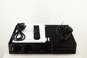 Top of a used Naim Supernait 3 Integrated Amplifier in a black finish showing Mains Cable, Remote, 2x Batteries, Schuko Cable and Manual