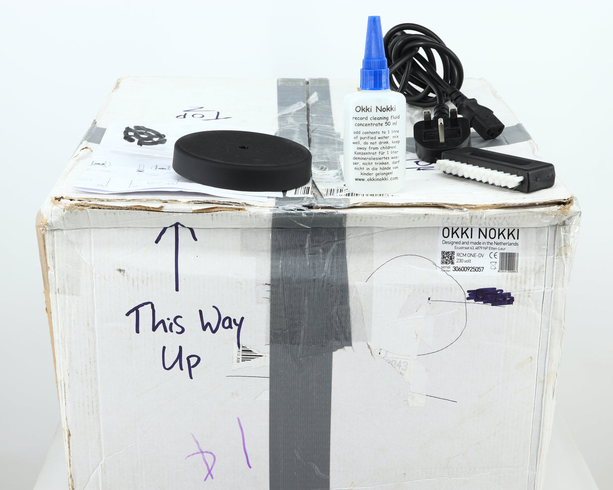 Box for a used Okki Nokki One Record Cleaning Machine in a black finish showing Manual, Cleaning Fluid, Brush and Mains Cable  
