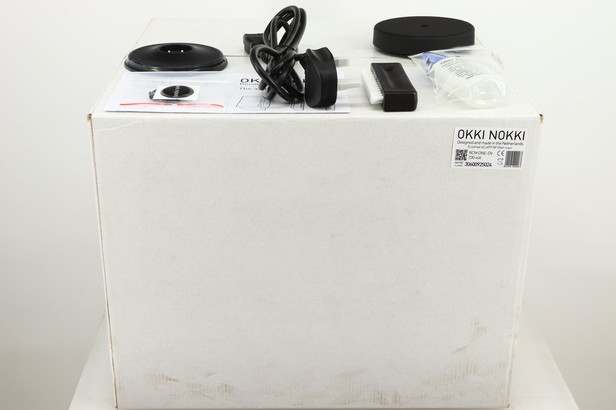 Box for a used Okki Nokki One Record Cleaning Machine in a black finish showing Mains Cable, Logo, Brush, Cleaning Fluid and Manual
