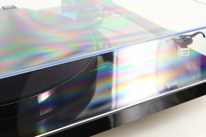 Close up view of a used Rega Planar 1 ECO Turntable in Black Gloss finish showing some scratching on the lid on the front side