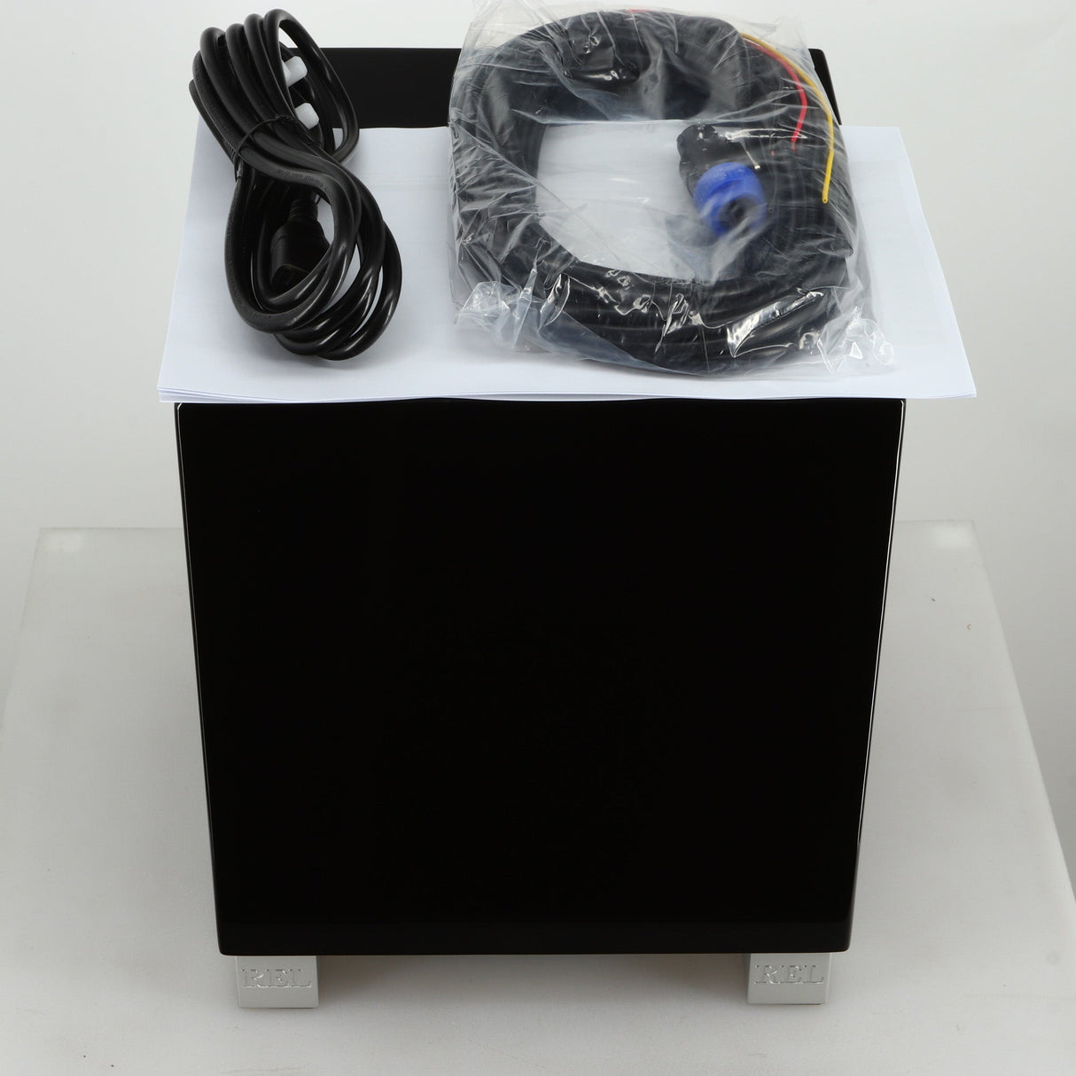 Top view of a REL T5i Subwoofer with a piano black finish showing mains cable, hi-level cable and manual
