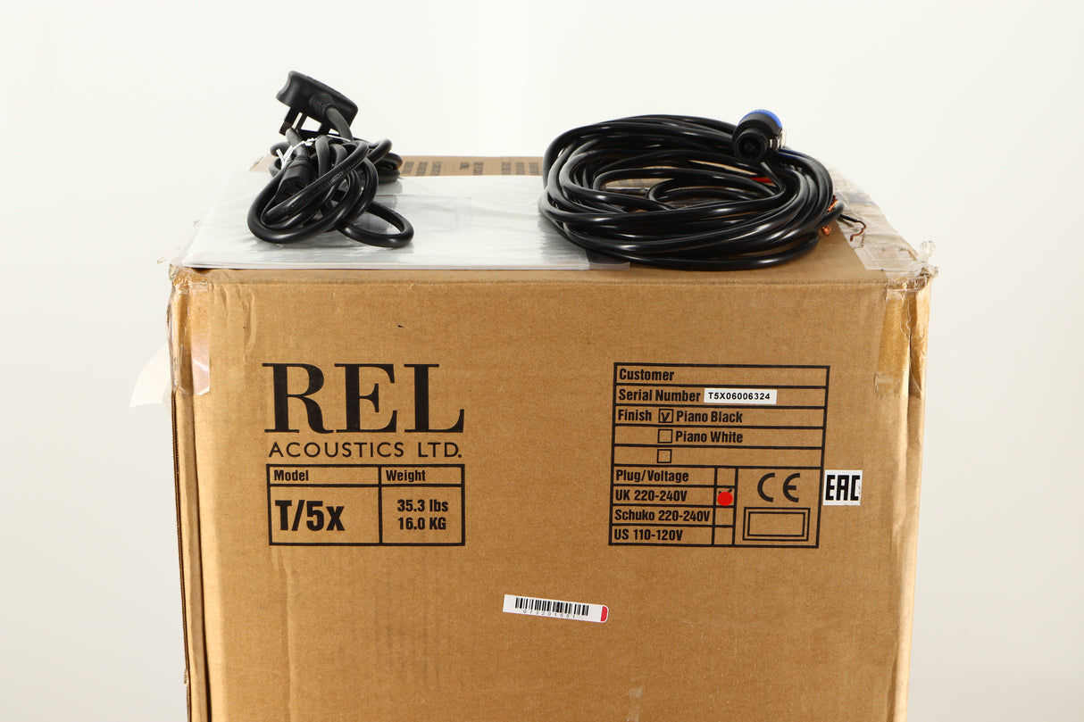 Box of a used REL T5X Subwoofer in Piano Black finish showing mains cable, manual, and hi level cable 