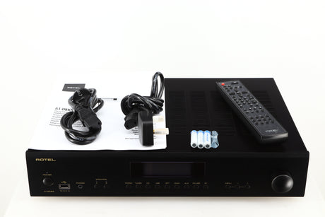 Top of a used Rotel A14 MKII Integrated Amplifier in a black finish showing Mains Cable, Batteries, Remote, Schuko Cable and Manual