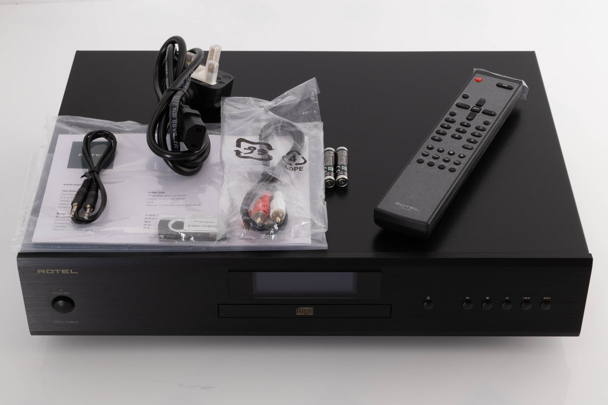 Top of a used Rotel CD11 MKII CD Player in a Black finish showing Remote, Batteries, Interconnect Cable, AUX Cable, Mains Cable, USB Stick and Manual