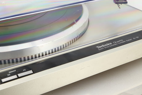 Close up view of a used Technics SL-Q2 Direct Driver Turntable in Silver showing some scratching on the turntable and the lid