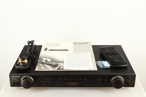 Top of a used Technics SU-C1000M2 Pre Amplifier in a black finish showing Power Cable, Manual, Remote and Batteries