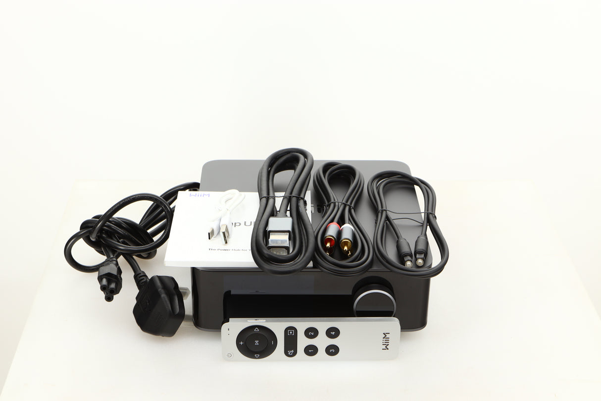 Top of a used Wiim Amp Ultra Streaming Amplifier in a grey finish showing Remote, Manual, Power Cable, USB Cable, Interconnect Cable, HDMI Cable and Optical Cable
