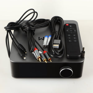 Top of a used Wiim Ultra Streamer showing HDMI Cable, Optical Cable, Interconnect Cable, 2x Batteries, Remote and Phono Ground Adaptor