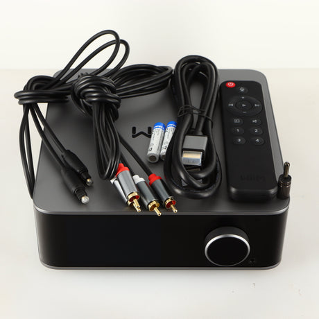 Top of a used Wiim Ultra Streamer showing HDMI Cable, Optical Cable, Interconnect Cable, 2x Batteries, Remote and Phono Ground Adaptor