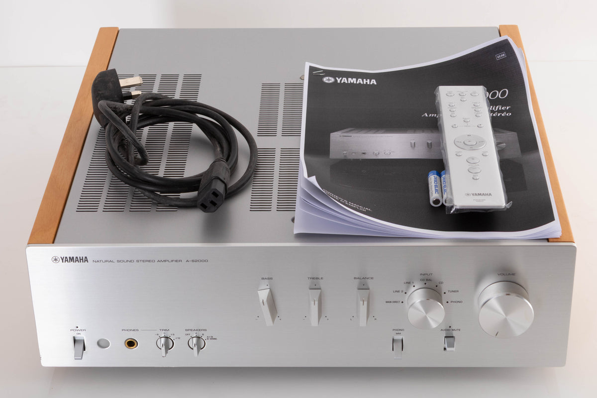 Top of a used Yamaha A-S2000 Integrated Amplifier in a Silver finish showing Mains Cable, Remote, Batteries and Manual